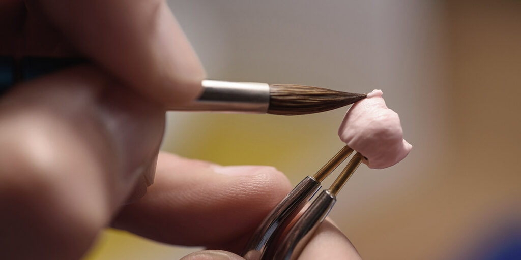 Man painting dental crown with paint brush UK vs overseas dental labs